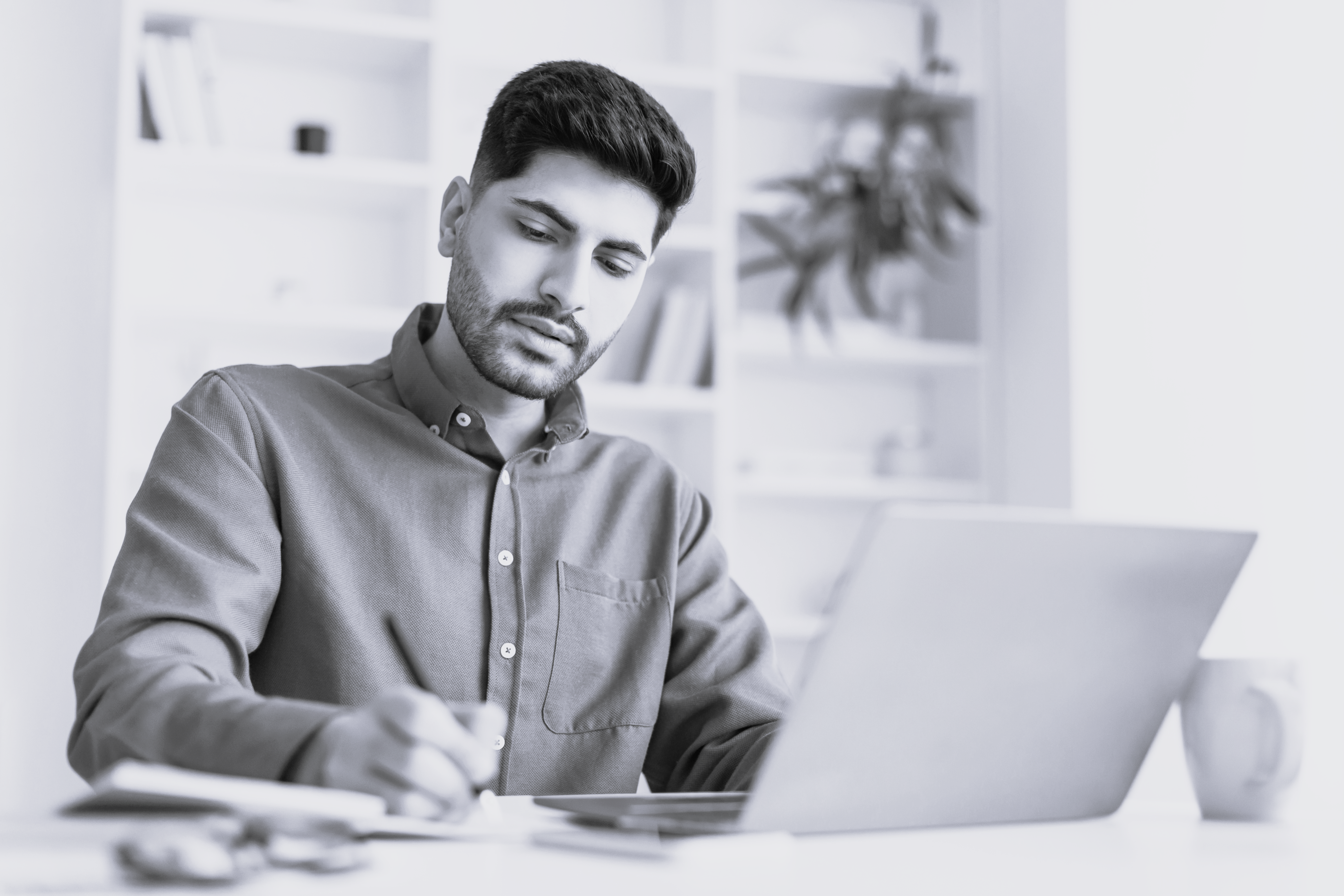 Ung mand studerer på bærbar og skriver i notesblok