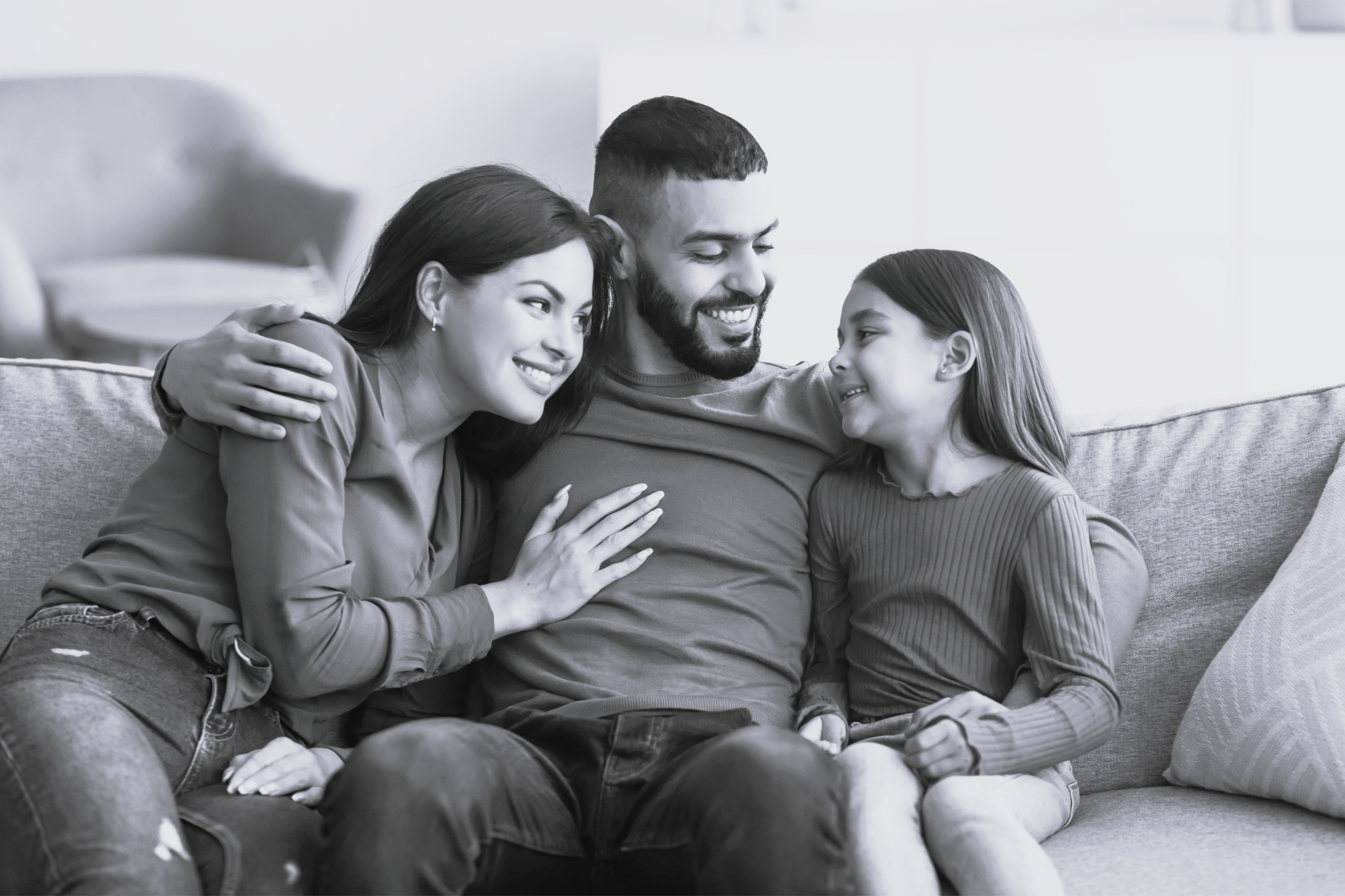 multietnisk familie sidder sammen på sofa og smiler til datter