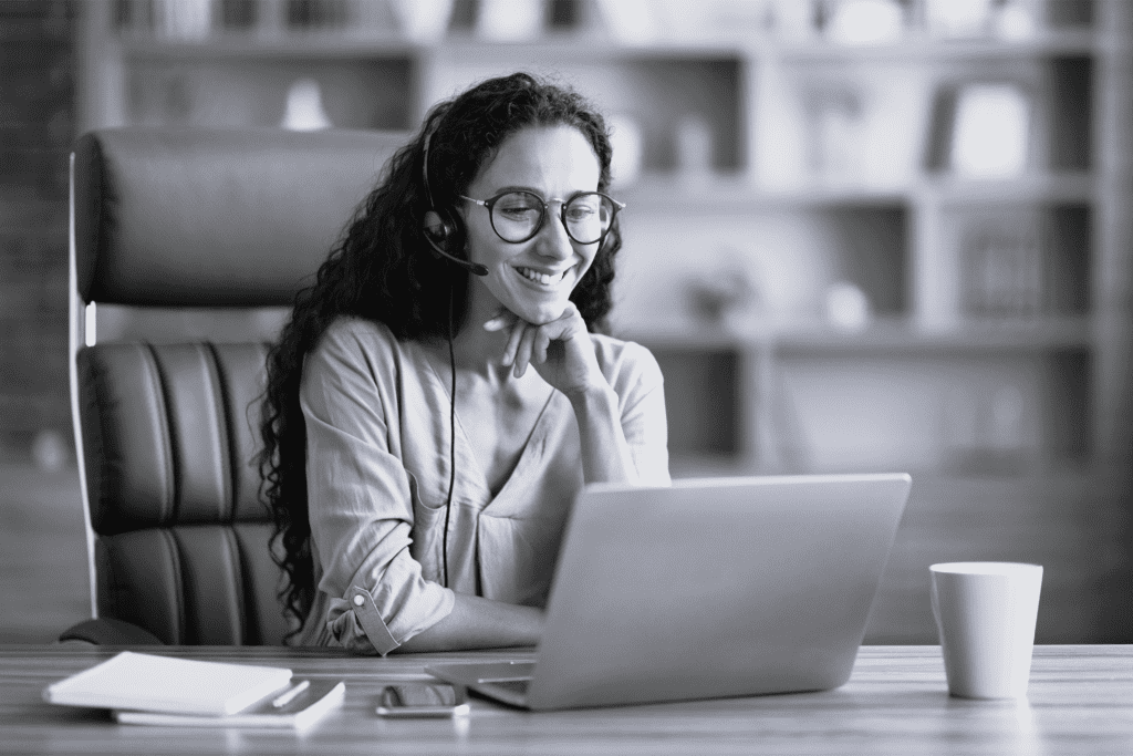 Ung kvinde sidder i kontor med hovedtelefoner på og studerer på bærbar