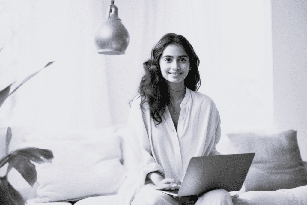 Ung pige sidder med bærbar og smiler